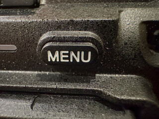 Close-up of button labeled MENU on black surface of device. Button stands out against texture that appears slightly rough and matte.