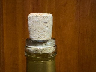 Close-up of a cork stopper made from cork wood, inserted into a bottle. The cork has a characteristic texture and light color, with the bottle set against a wooden background.