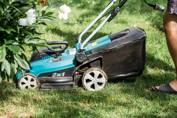 Fototapeta premium A man with a lawn mower mows the grass in the backyard. Agricultural machinery for garden maintenance. The banner.