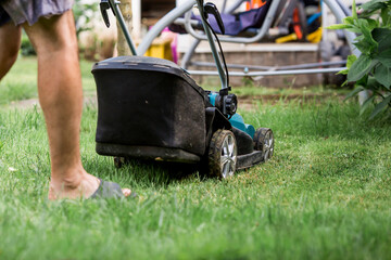 Obraz premium A man with a lawn mower mows the grass in the backyard. Agricultural machinery for garden maintenance. The banner.