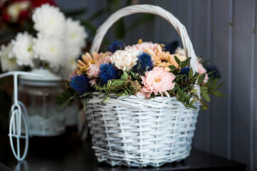 A beautiful, delicate bouquet of flowers in a white wicker basket in the interior. Close-up. Decoration.