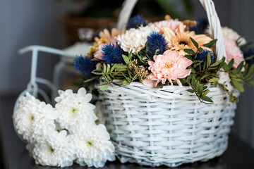 A beautiful, delicate bouquet of flowers in a white wicker basket in the interior. Close-up. Decoration.