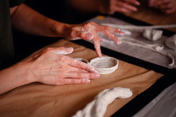 Close-up of hands carefully molding clay into a shape on a table. The image highlights the artistic process and the tactile nature of working with clay.