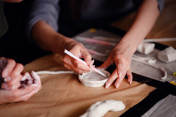 Close-up of hands using sculpting tools and shaping clay on a table. The image showcases the detailed process of crafting and artistic creation.