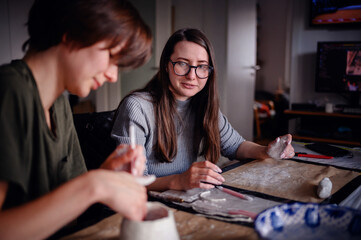 Two women engaged in a clay sculpting project, conversing and sharing a creative moment. The image...