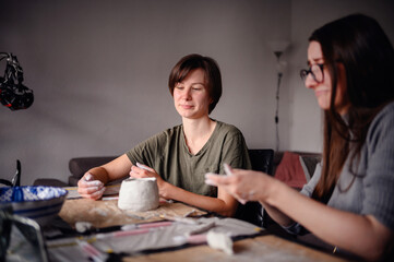 Two women smiling and enjoying themselves while working on a clay pottery project. The scene highlights creativity and a joyful, relaxed atmosphere.