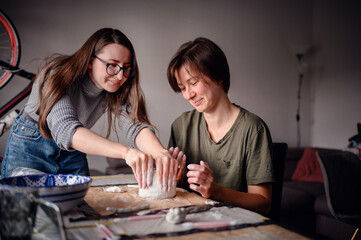 Fototapeta premium Two women working together on a clay pottery project, focusing on shaping and detailing the piece. The scene highlights collaboration, creativity, and concentration.