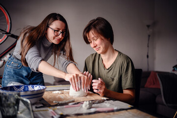 Two women working together on a clay pottery project, focusing on shaping and detailing the piece....