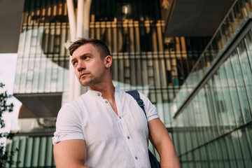 A man in a white shirt standing in front of a modern architectural building with glass and curved...