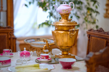 Beautiful antique copper samovar on the table in an old hut. Tea accessories on the table by the window.