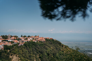 Panoramic view of Sighnaghi, Georgia, a historic town with red rooftops and lush green hills, overlooking the Alazani Valley on a clear summer day