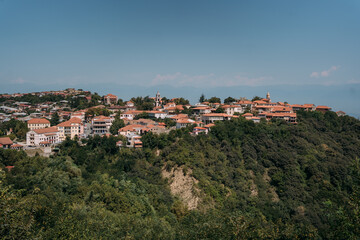 Fototapeta premium Panoramic view of Sighnaghi, Georgia, a historic town with red rooftops and lush green hills, overlooking the Alazani Valley on a clear summer day