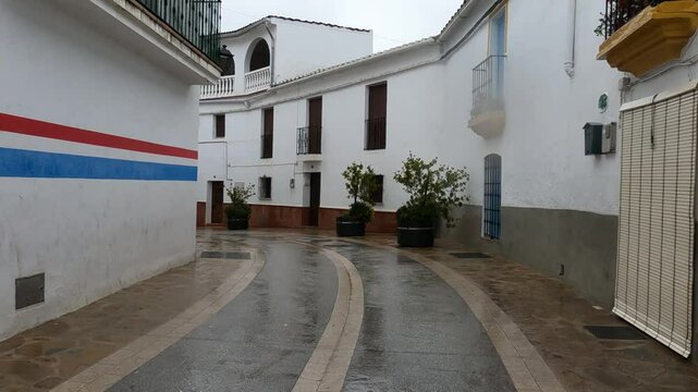 Gaucin, Spain - January 26, 2025 -A narrow, wet street in a quiet residential area with white walls, colorful accents, potted plants, and a peaceful atmosphere after rain.