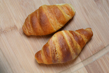 Two golden-brown croissants are displayed on a wooden cutting board