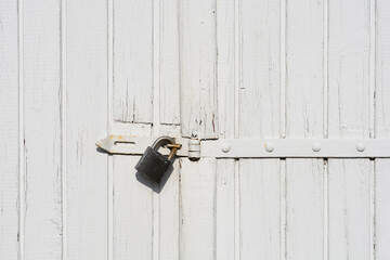 Detail of a weathered white wooden door with peeling paint secured by a padlock