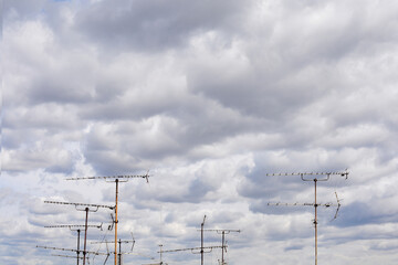 A group of old television antennas point upwards against a cloudy sky, evoking a sense of nostalgia and technological obsolescence