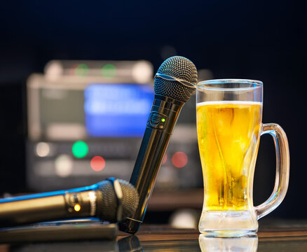 A close-up shot of two microphones and a glass of beer on a table in a japanese karaoke bar captured with a shallow depth of field to emphasize the subjects and atmosphere for karaoke enthusiasts.