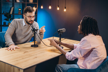 Male podcasters discussing content while recording radio show in soundproof professional studio...