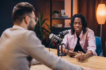 Two male podcasters are recording a new episode of their podcast in a studio, using professional...
