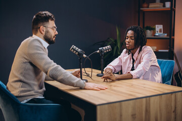 Podcasters talking animatedly while recording, seated in sleek studio with professional microphones...