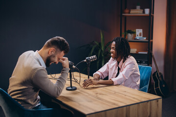 Male podcasters recording audio, sharing laughter in professional broadcast setting