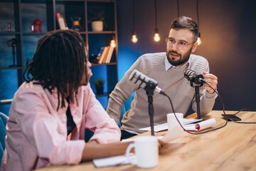 Podcasters conversing while recording audio in professional broadcasting studio