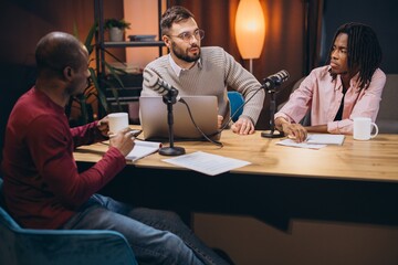 Three radio hosts recording a podcast in a professional studio, engaging in discussion and sharing insights with their audience