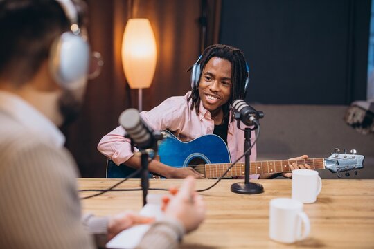 Young musician playing guitar and singing during a podcast interview in a recording studio