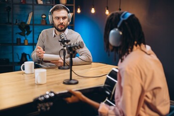 Two people recording a music podcast in a professional studio, radio host interviewing a musician playing guitar