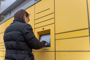 A woman stands in front of a packing station in Germany and takes a package out of a compartment