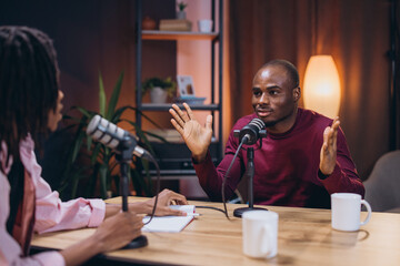 Two African American content creators are recording a podcast episode in a professional studio, using microphones and other equipment