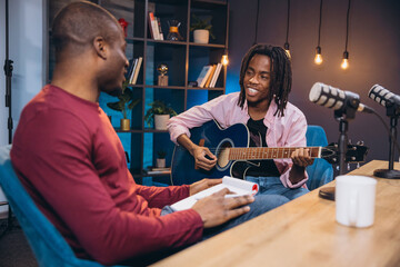 African American musician performing acoustic guitar while engaging with interviewer during podcast...