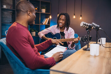 African American musician playing guitar during a podcast interview with a radio host in a...