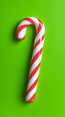 Festive red and white candy cane on vibrant green background. Concept of holiday cheer, Christmas treats, festive sweets, joyful celebration. Vertical shot