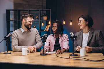 Three podcasters sitting around a table, recording an engaging audio podcast in a modern studio,...