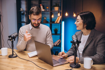 Two content creators recording their podcast in a studio, using professional microphone and laptop