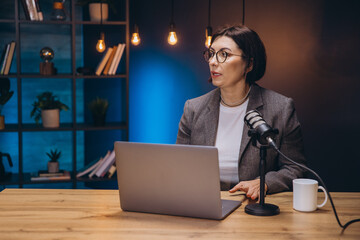 Elegant woman recording a podcast in her studio using a laptop and a professional microphone