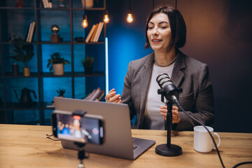 Mature content creator speaking animatedly, recording podcast with professional mic and laptop in...