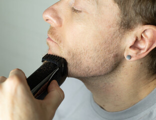 A man trims his beard with a trimmer. An electric razor trimming a beard.