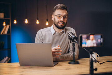 Young man recording a podcast in his home studio using a professional microphone, laptop and smartphone