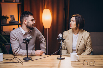 Podcast hosts collaborating, speaking into microphones inside modern recording studio