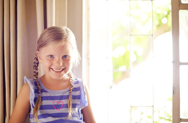 Portrait, smile and girl child in house for relax, weekend and break in living room. Cute face, young and happy kid by window to chill, adorable and positive for development or growth in Switzerland