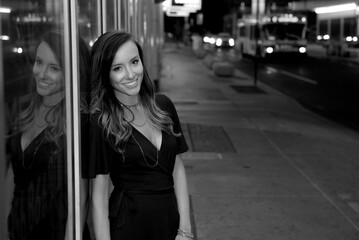 Beautiful young woman poses wearing short black dress and standing near street with bright lights overhead in tunnel