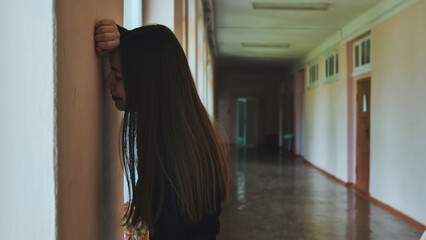 Lonely teenage girl in school corridor, overwhelmed by bullying and anxiety during school hours