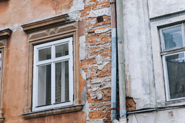 The old building with windows, a column and a capital is in a state of destruction, exposing red bricks from under the falling plaster. Decline and aging concept.