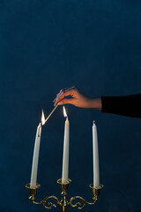 A young woman illuminates the candles in a candleholder.