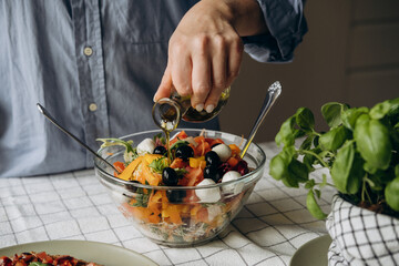 Women's hands cooking and mixing salad with tomato  olives mozzarella vegetables arugula dressing with balsamic vinegar and olive oil in a large bowl a healthy balanced meal 