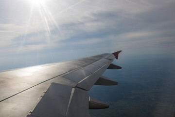 Fototapeta na wymiar View through the flying plane window on a beautiful blue skyscape, shining sun, and airplane wing. Travel time and transport concept.