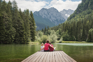 Mother sitting on the dock hugging her children, daughter, and son, enjoying the majestic mountain and lake view. Family time and vacation concepts.