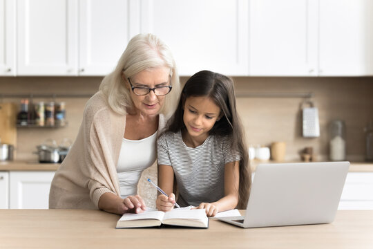 Senior granny assist school age granddaughter with homework help to study grammar rules from textbook. Friendly aged female tutor give personal lesson to little girl explain learning material at home